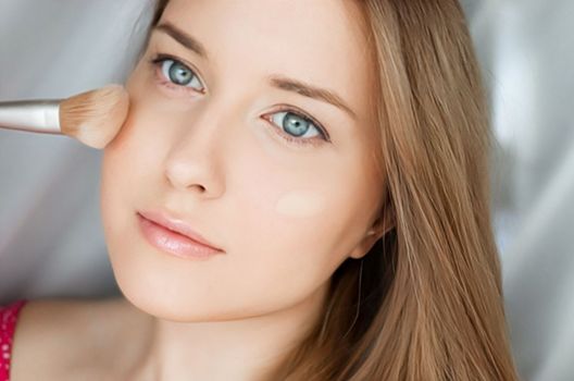 Beautiful woman applying liquid make-up foundation on her skin with make-up brush.