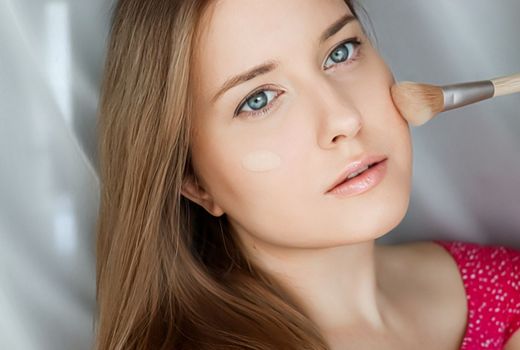 Beautiful woman applying liquid make-up foundation on her skin with make-up brush.