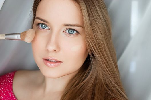 Beautiful woman applying liquid make-up foundation on her skin with make-up brush.