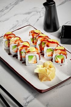 Appetizing sushi rolls with cream cheese, avocado and masago roe topped with butterfish fillet dressed with Japanese mayonnaise and unagi sauce served on plate with pickled ginger and soy sauce