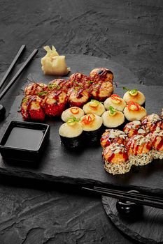 Three types of baked rolls with fish and seafood topped with creamy cheese hats, unagi sauce, mayonnaise drops and vegetable shavings served for two with soy sauce and pickled ginger on black board