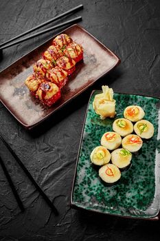 Delicious baked uramaki with salmon dressed with unagi sauce and warm makizushi with creamy cheese hat garnished with mayonnaise drops and vegetable shavings served with pickled ginger. Dinner for two