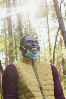 Handsome african american man wearing casual clothes and medical mask smiling happy walking in city park - end pandemic