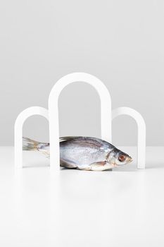 Dried salty roach lying under arches on white and gray background. Abstract showcase with geometric shapes for presentation of popular fish snack