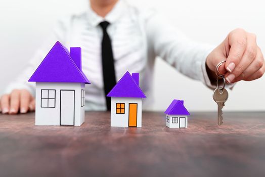 Businesswoman holding keys. olored paper houses standing on desk.