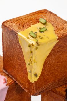 Closeup of browned crispy crust cube shaped croissant with delicate pistachio sauce and nut crumbs on white background. Delicious French style sweet viennoiserie pastry