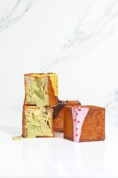 Three freshly baked cube shaped croissants, one sliced with pistachio cream filling and two whole with berry glaze and chocolate ganache on light background. French style sweet viennoiserie pastry