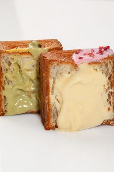 Two halves of light, flaky and delicate cube shaped croissants with pistachio cream and vanilla custard decorated with colorful glaze and candied berry crumbs. Delicious sweet French style pastries