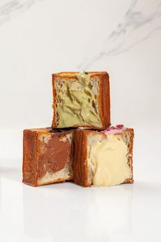 Three halved cubed puff pastry croissants with crispy browned crust and fillings of vanilla custard, light pistachio and chocolate cream. Creative variety of traditional sweet viennoiserie pastry