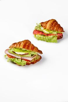 Two appetizing puff French croissant sandwiches stuffed with fried eggs, ham slices, salami, cheese, salted salmon, fresh tomatoes and lettuce isolated on white. Delicious hearty breakfast