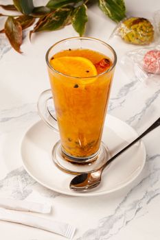 Vitamin fragrant fruit and berry tea from ripe sea buckthorn and orange with cinnamon stick in glass cup served with sweet pastries. Healthy and immune-boosting drinks concept