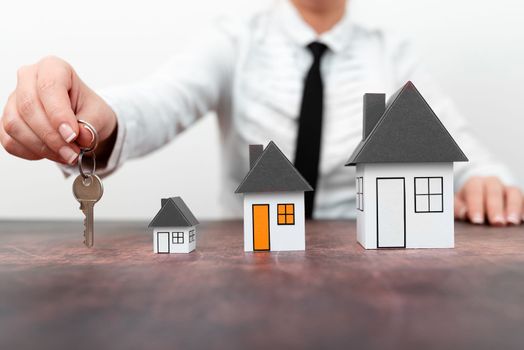 Businesswoman holding keys. olored paper houses standing on desk.