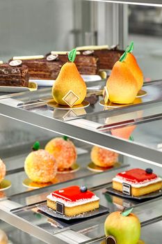 Various fresh baked sweet cakes and fruit shaped pastries presented on showcase in confectionery. Sweet tooth concept