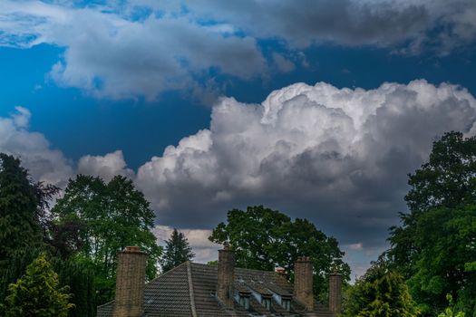 The roof of the house and the tree with the backdrop of a beautiful blue sky with a cloudy cloud background