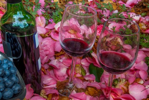 bottle, wine glasses with blueberry in rose garden.