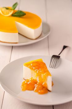 Slice of Italian cheesecake on shortcrust pastry with delicate vanilla souffle and sourish layer of passion fruit puree served with orange jam on white wooden table. Treat for tea. Popular dessert