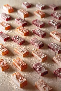 Delicate homemade jelly candies of natural fruit and berry juice sprinkled with powdered sugar arranged on white wooden table. Concept of healthy organic sweets