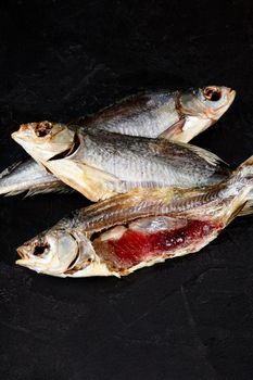 Two whole salted air-dried roach fish and one peeled fish with caviar on black background. Popular natural savory snack