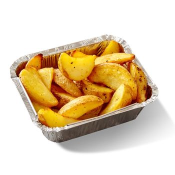 Appetizing golden crispy baked potato wedges served in aluminium foil container isolated on white background. Concept of popular side dish and fast food snack. Takeaway food