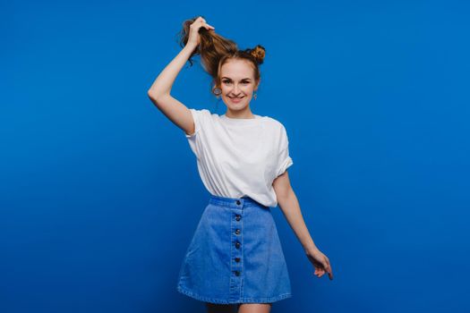 A young stylish girl pulls her hair on a blue background, a Model pulls her long hair