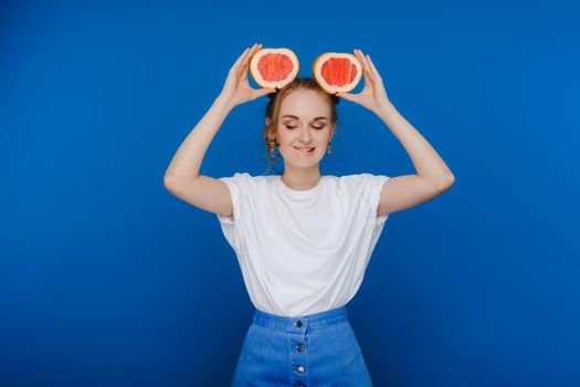 Surprised, the laughing girl holds the grapefruit like ears. Vegan lifestyle. Smiling woman , eating concept.Diet organic , weight loss and healthy food. Smoothies and fresh juice