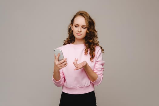 A happy young girl holding a phone looks into it and smiles.