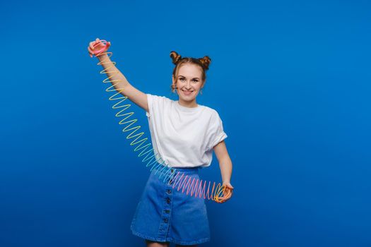 Beautiful young girl playing with a rainbow slinky, a toy of her childhood on a blue background.