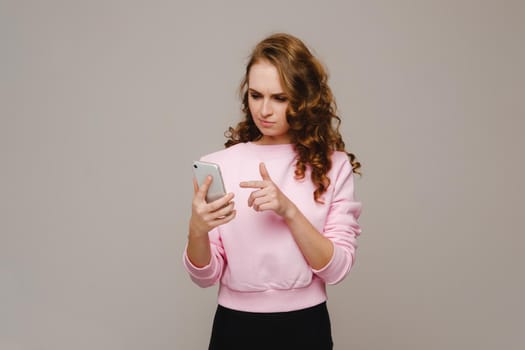 A happy young girl holding a phone looks into it and smiles.