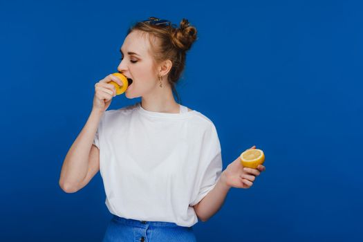 a young beautiful girl standing on a blue background holding lemons in her hand and biting