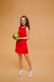 A beautiful girl in glasses and a red dress holds a watermelon in her hands.