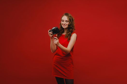 a smiling young woman with wavy hair holds a strawberry and photographs it, holding a delicious fresh strawberry on a bright red background.