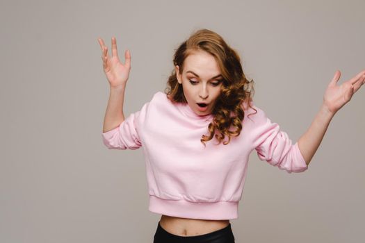 A beautiful girl on a gray background holds her head and screams emotionally.