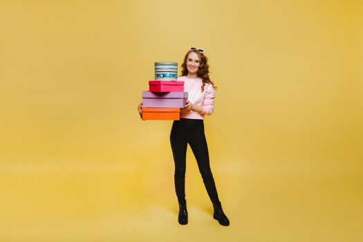 A happy young woman with colorful paper boxes after shopping isolated on an orange Studio background. Seasonal sales, purchases, spending money on gifts.