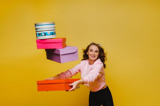 A happy young woman with colorful paper boxes after shopping isolated on an orange Studio background. Seasonal sales, purchases, spending money on gifts.