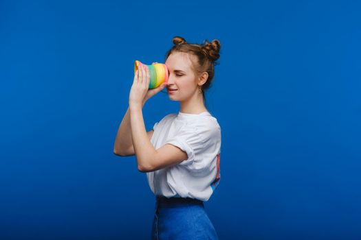 Beautiful young girl playing with a rainbow slinky, a toy of her childhood on a blue background.