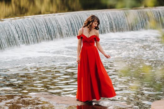 girl in a long red dress near the lake in the Park at sunset