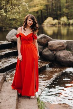 girl in a long red dress near the lake in the Park at sunset