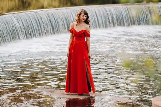 girl in a long red dress near the lake in the Park at sunset