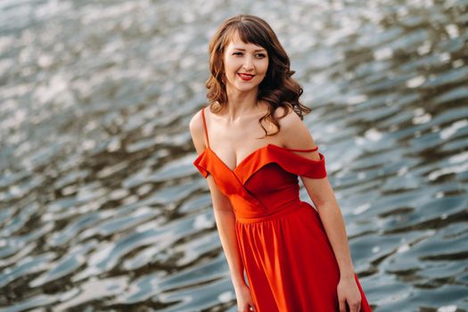 girl in a long red dress near the lake in the Park at sunset