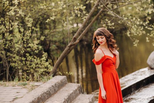 girl in a long red dress near the lake in the Park at sunset