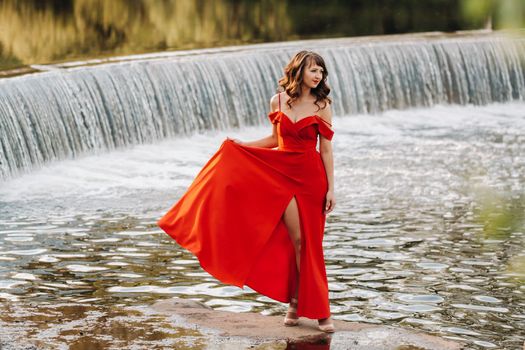 girl in a long red dress near the lake in the Park at sunset