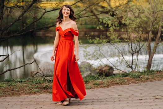 girl in a long red dress near the lake in the Park at sunset