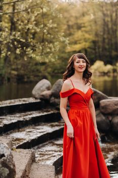 girl in a long red dress near the lake in the Park at sunset