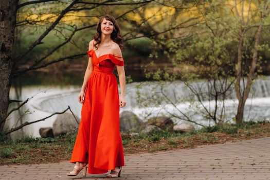 girl in a long red dress near the lake in the Park at sunset