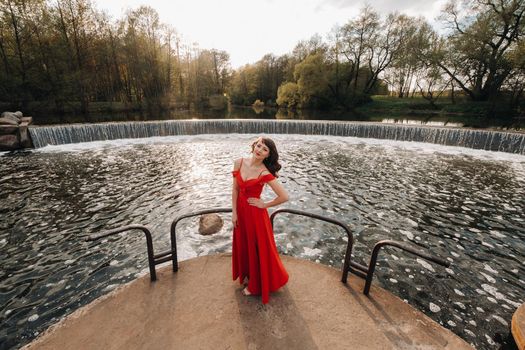 girl in a long red dress near the lake in the Park at sunset