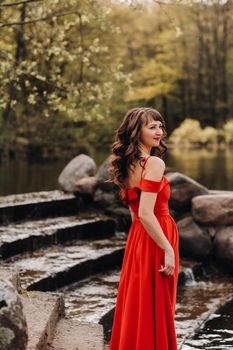 girl in a long red dress near the lake in the Park at sunset