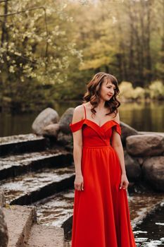 girl in a long red dress near the lake in the Park at sunset