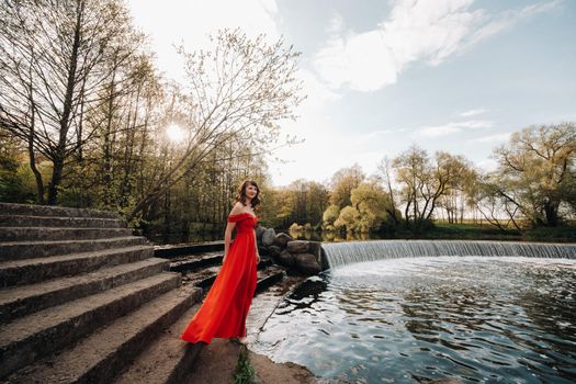 girl in a long red dress near the lake in the Park at sunset