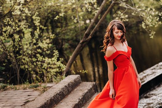 a young beautiful girl with long brown hair , in a long red dress comes down the stairs near the lake