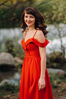 girl in a long red dress near the lake in the Park at sunset